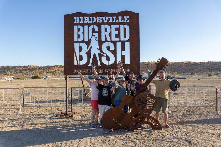 Happy festival-goers posing beneath the Birdsville Big Red Bash welcome sign in the desert outback.